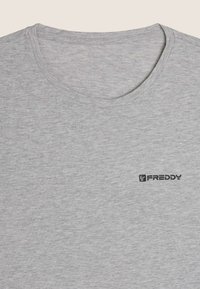 Camiseta gris de manga corta hecha de tela suave, con cuello redondo y un pequeño logo negro "FREDDY" en el pecho. Textura lisa.