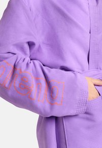 Indumento in pile viola con un grande logo arancione, texture a coste sui polsini e una cintura in vita per una vestibilità aderente.