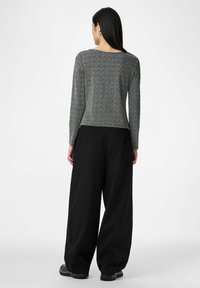 Juodos plačios kelnės derinamos su tekstūruotu pilku ilgomis rankovėmis palaidine. Palaidinėje yra apvali iškirptė ir prigludęs siluetas, paryškinantis liemenį.