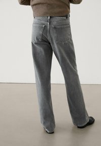 Jeans in denim grigi con un design a gamba dritta, dotati di due tasche posteriori e chiusura con zip, poggiati su una superficie liscia.