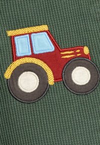 Gestickter roter Traktor auf einem grünen gerippten Stoffhintergrund. Verfügt über blaue Fenster, gelbe Akzente und runde schwarze Räder mit weißen Mitteln.