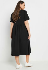 Musta puuvillamidi-mekko lühikeste varrukatega, kogutud vöökoht, laienev seelik ja sile tekstuur; kantud valgete tossudega.