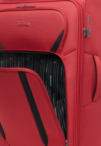 Czerwona walizka twarda z czarnymi akcentami, posiadająca zasuwaną komorę i teksturowany zewnętrzny materiał. Wnętrze ma czarne wykończenie z białym brandingiem.