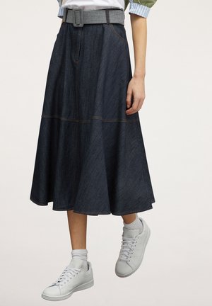 Denim midirok met een brede A-lijn, hoge taille, stoffen riem, gedragen met witte enkelsokken en witte sneakers.