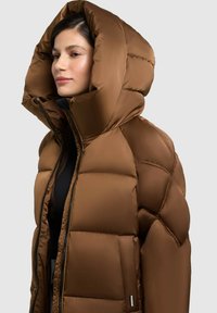 Giubbotto puffo marrone con cappuccio grande, texture trapuntata, chiusura con zip, tasche laterali e etichetta del logo sull'orlo. Finitura liscia e lucida.