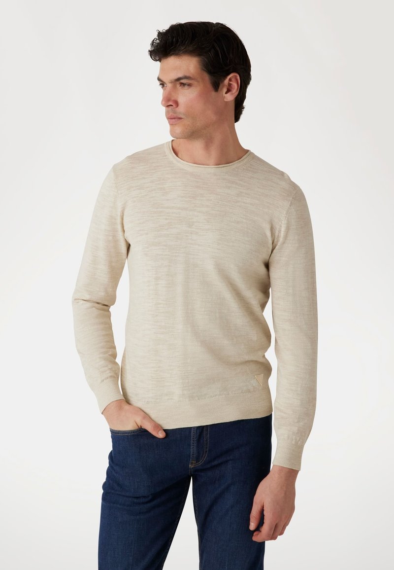 Hellebeige Pullover mit Rundhalsausschnitt, mit einem strukturierten Muster, gerippten Bündchen und Saum. Der Stoff wirkt weich und wird mit dunkelblauen Jeans kombiniert.