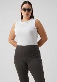 White ribbed sleeveless top paired with dark gray stretchy leggings. Model has long brown hair and wears angular sunglasses.
