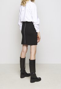 Schwarzer Minirock mit weißen Nähten, getragen mit einem weißen Langarmhemd und knielangen schwarzen Lederstiefeln mit dicker Sohle.