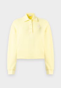 Polo de manga comprida amarelo pálido com três botões, punhos canelados e um pequeno emblema texturizado no peito esquerdo.