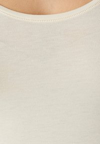 Light beige ribbed tank top with a rounded neckline, made from soft, stretchy fabric; features fine stitching along the edges.