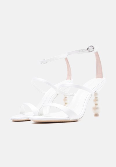 Λευκά ψηλοτάκουνα σανδάλια με λουράκια, τακούνια διακοσμημένα με πέρλες και λουράκια αστραγάλου με μικρές στρογγυλές ασημένιες αγκράφες.