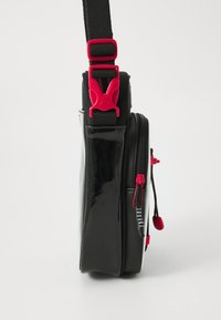 Borsa nera con finitura lucida, dettagli rossi, tracolla regolabile e chiusure con zip. Presenta tasche laterali e superficie testurizzata.