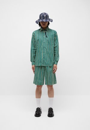 Green and ivory striped shirt with a matching short, paired with a navy floral bucket hat. Black shoes and white socks complete the outfit.