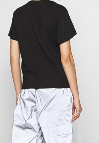 Svart t-shirt i bomull med korta ärmar och klassisk passform, med minimala sömmar. Bärs med ljusgrå cargobyxor.