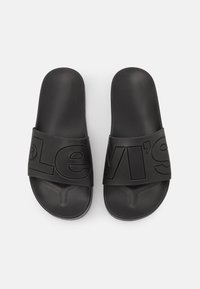 Sandales à enfiler en plastique noir avec une large bride embossée du logo Levi's, texture lisse et design à bout ouvert.