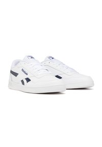 Zapatillas de cuero blanco con acentos en azul marino, puntera redonda, suela de goma plana y diseño clásico con cordones. Presenta el logo de Reebok en el lateral y la lengüeta.