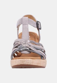 Harmaa mokka-sandaali ristiin menevien hihnojen, hopeisten yksityiskohtien ja punottu juuttipohjan kanssa. Varustettu säädettävällä nilkkahihnalla, jossa on solki.