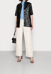Black leather short-sleeve shirt with shiny buttons, paired with cream wide-leg trousers. Accessory: small black handbag and stiletto sandals.