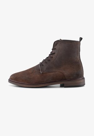 Bottine en daim marron avec un bout arrondi, design à lacets et semelle marron contrastante. Présente une petite boucle en haut pour un enfilage facile.