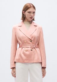 Ροζ διπλό�ς σακάκι με ζώνη στη μέση, χρυσά κουμπιά και γιακά με εγκοπή. Το ύφασμα έχει μια λεπτή υφή, συνδυασμένο με ένα ανοιχτόχρωμο τοπ.