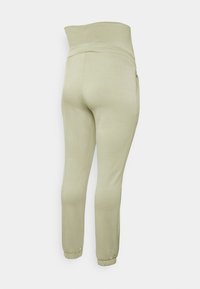 Calças de jogging em tecido suave verde claro, com uma cintura alta, punhos elásticos e bolsos laterais. Textura suave com um corte ajustado.