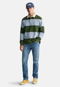 Green and light blue striped long-sleeve polo with a beige collar, paired with light blue jeans and yellow sneakers, accentuated by a blue cap.