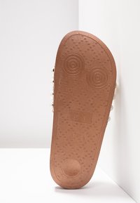 Semelle de chaussure en caoutchouc marron avec un motif texturé, comportant deux indentations circulaires. Le côté inclut des accents surélevés et des marquages de taille.