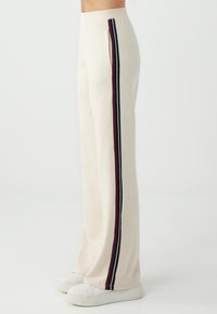 Damen-Sweatpants mit weitem Bein aus cremefarbenem Stoff, ausgestattet mit Seitentaschen, einem hohen Bund und vertikalen Streifen in Marineblau und Burgunderrot.