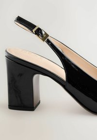 Černý lakovaný kožený slingback boty na podpatku s tlustým podpatkem a zlatou přezkou na pásku, umístěné na neutrálním pozadí.