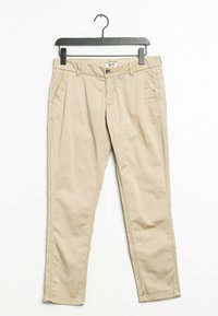 Beige bomulls chinos på en svart galge. Funktionerna inkluderar framfickor, slät textur och raka ben med minimala sömmdetaljer.