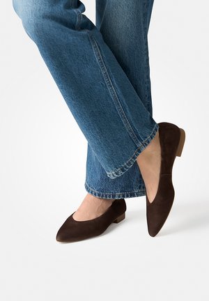 Person wearing dark brown suede pointed flats and blue denim jeans with slightly cropped hems against a plain background.
