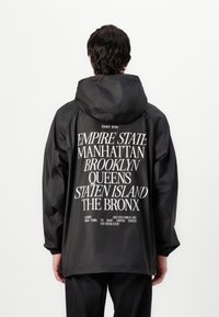 Black hooded jacket featuring large white text on the back listing New York boroughs. Lightweight, with elastic cuffs and a relaxed fit.