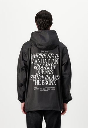 Schwarze Kapuzenjacke mit großen weißen Buchstaben auf dem Rücken, die die Stadtteile von New York auflisten. Leicht, mit elastischen Bündchen und lockerer Passform.