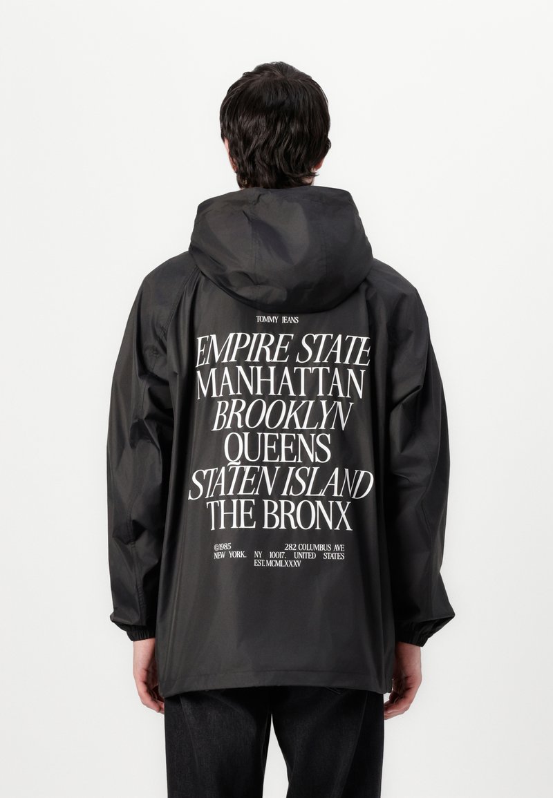 Black hooded jacket featuring large white text on the back listing New York boroughs. Lightweight, with elastic cuffs and a relaxed fit.