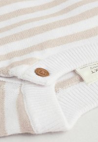 Lekki sweter w poziome beżowe i białe paski, z ryżowym splotem i małym drewnianym guzikiem przy kołnierzu.