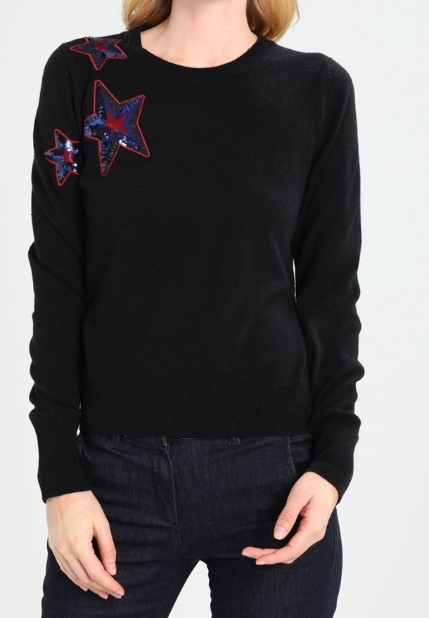 Schwarzer Strickpullover mit drei gestickten Sternen in Rot und Blau sowie Paillettenakzenten an der linken Schulter. Gerippter Saum und Bündchen.
