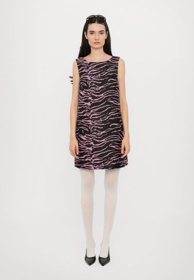 Ein ärmelloses Kleid aus schwarzem Stoff mit pinken Tigerstreifen, knielang, kombiniert mit weißen Strumpfhosen und schwarzen spitzen Schuhen.