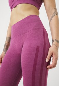 Paarse high-waisted leggings met een textuurafwerking, voorzien van verticale gestreepte accenten en een strakke pasvorm. Het materiaal lijkt rekbaar.