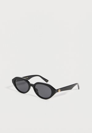 Black cat-eye sunglasses with dark lenses and gold logo detail on the temple, set against a plain white background.