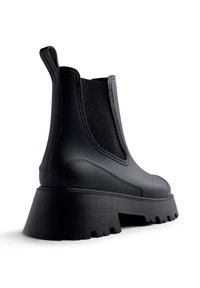 Bottines Chelsea noires en matériau caoutchouteux, avec des panneaux latéraux en élastique, une semelle épaisse et texturée au talon pour une meilleure adhérence.