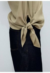 Beige, gestrikt shirt gemaakt van zachte stof, gedragen met donkere denim jeans met een achterzak. Het shirt is geknoopt op de taille.