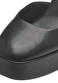 Gros plan d'une chaussure plateforme en cuir noir avec un bout arrondi et une semelle épaisse.