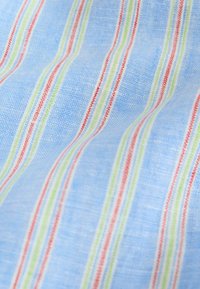 Tissu bleu clair avec une surface texturée présentant un motif répétitif de rayures verticales rouges, blanches et vertes.