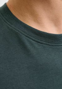 Tela de camiseta verde oscuro con una textura suave y un escote en forma de barco. Las costuras son visibles a lo largo del cuello y la zona de los hombros.