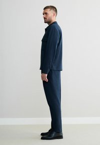 Dark blue tailored jacket with flap pocket and matching trousers, textured fabric, straight fit, paired with black lace-up shoes.