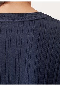 Gros plan sur le haut du dos d'une personne portant un pull en maille côtelée bleu marine avec des rayures verticales texturées.