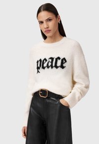 Biały, miękki sweter z czarnym napisem "pokój", okrągły dekolt, ściągacze na rękawach. Połączony z eleganckimi czarnymi skórzanymi spodniami i szerokim paskiem.