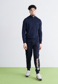Námornícky zipsový sveter a zodpovedajúce tepláky so značkou Timberland, vyrobené z mäkkého materiálu, doplnené textúrovaným povrchom.