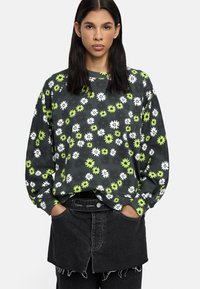 Czarna bluza z białym i neonowozielonym wzorem kwiatowym, luźny krój, okrągły dekolt i długie rękawy. W zestawieniu z czarną spódnicą dżinsową.