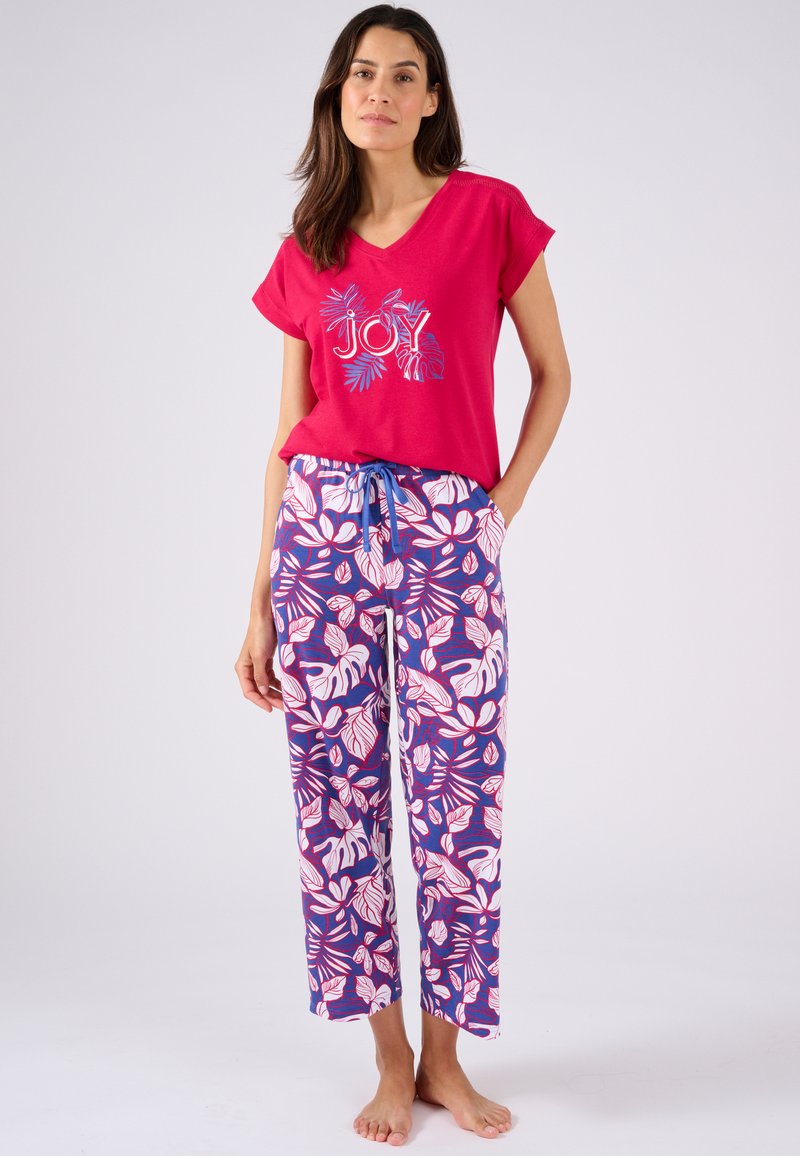 Blusa rosa de escote en V con gráfico de "JOY" y acentos azules, combinada con pantalones sueltos y estampados en diseño floral púrpura, blanco y rojo.